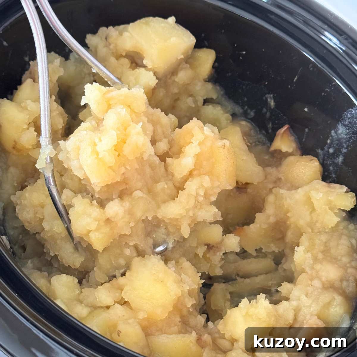 Cream Cheese Crock-Pot Mashed Potatoes — Slow Cooker Recipe 5 Cooked potatoes being mashed with a potato masher in the base of a crock-pot.
