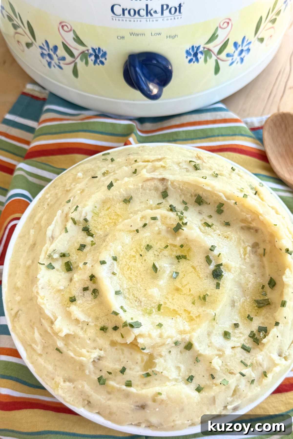 Cream Cheese Crock-Pot Mashed Potatoes — Slow Cooker Recipe 7 Creamy slow cooker mashed potatoes topped with melted butter and chives in a large bowl with a slow cooker behind it.