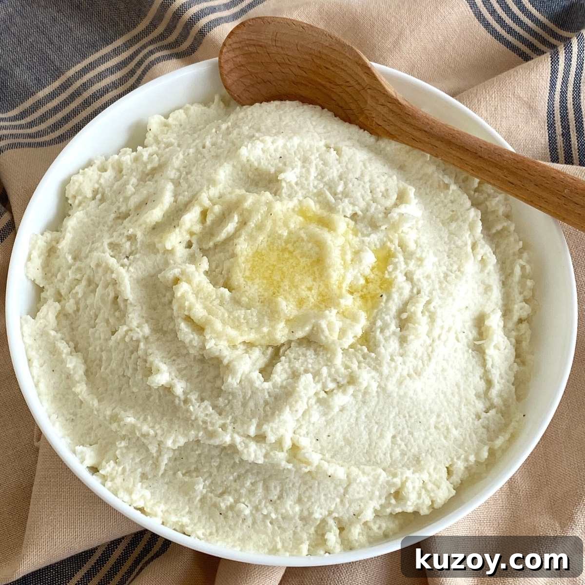 Frozen cauliflower mash in serving bowl with wooden spoon.