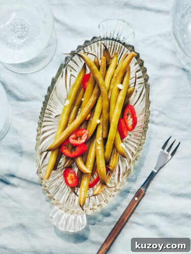 Plate of pickled green beans and peppers on a table with sparkling water on the side