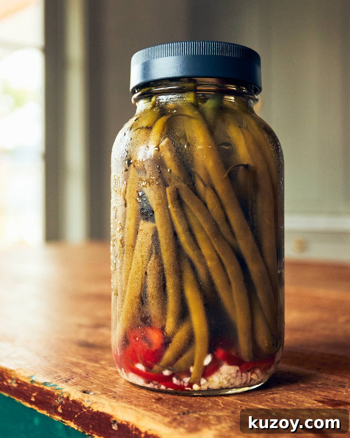 Jar of quick pickled green beans sitting on a wooden table in a kitchen