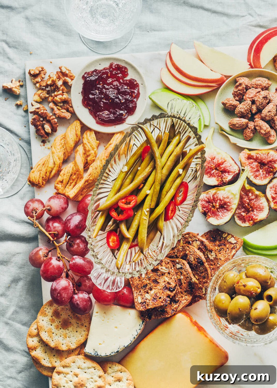 Snack board with fruit, crackers, olives, jam and pickled green beans on a table