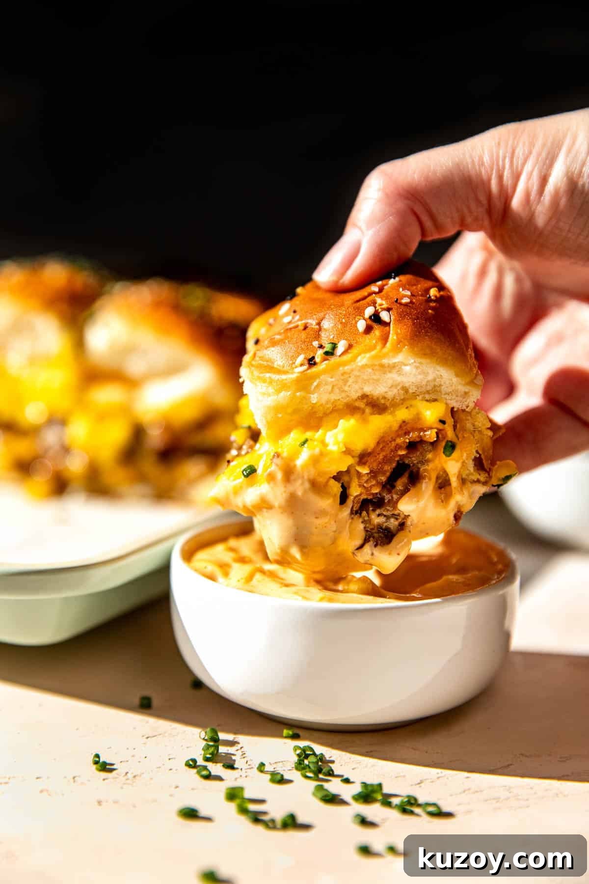 a womans hand holding a breakfast sandwich dunking it in sriracha mayo. 