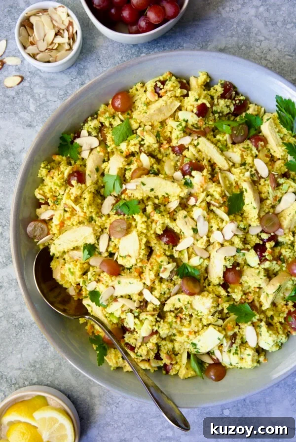 Chicken Couscous Salad in gray bowl with serving spoon with bowl of sliced almonds, whole grapes and lemon wedges.