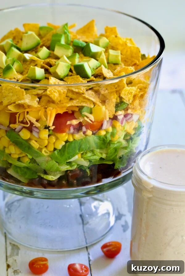 Southwestern Layered Salad in glass footed bowl with salad dressing in glass jar.