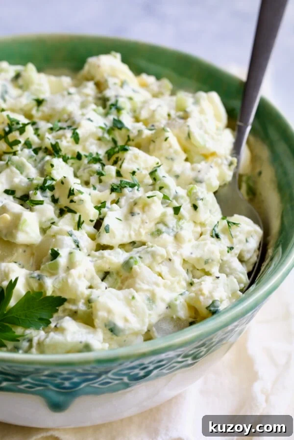 Creamy Potato Cucumber Salad in green and white serving bowl with serving spoon.