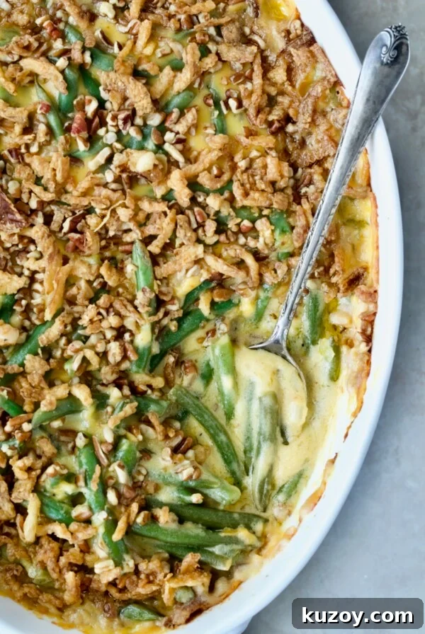 Cheesy Green Bean Casserole in white oval gratin dish with serving spoon.