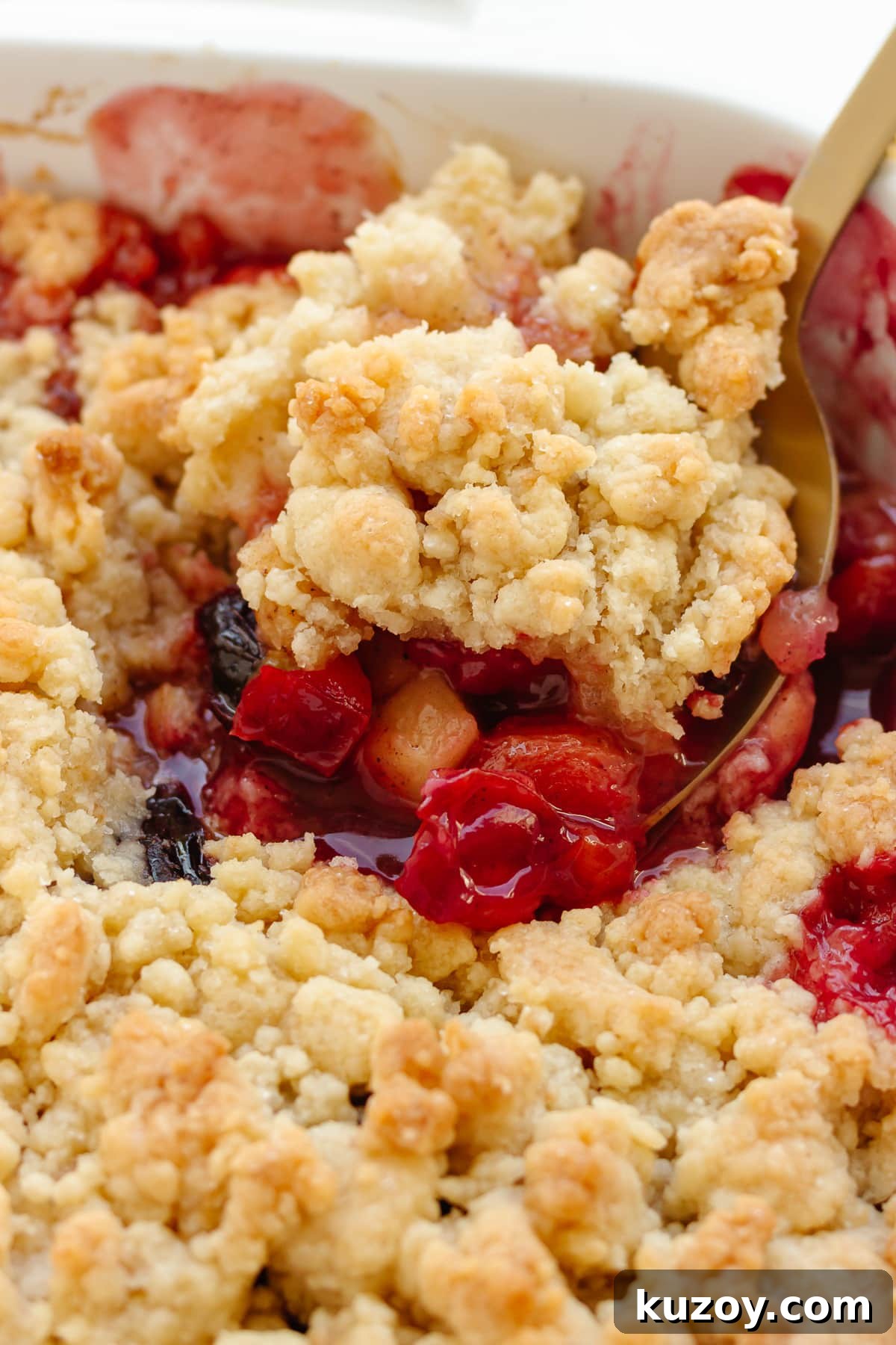 Scoop of plum and apple crumble being lifted from baking dish.