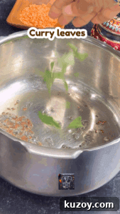 Fresh curry leaves being added to a stainless steel pot for red lentil curry.