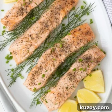 Close up of a platter of salmon filets with lemon and herbs on a table.