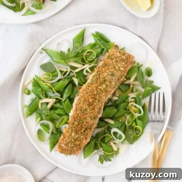 A pistachio crusted salmon filet on a bed of bright green sugar snap peas with a fork.