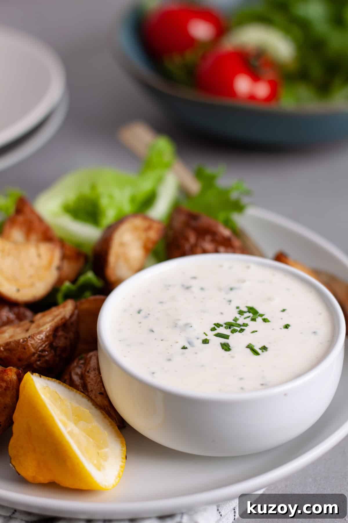 A small bowl with horseradish aioli topped with fresh chives on a plate with crispy fried potatoes.