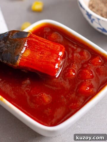 A small bowl of pineapple bbq sauce with a brush inside and a chopped pineapple in the background.