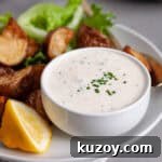 A closeup of horseradish aioli in a small bowl on a platter of crispy roasted potatoes.