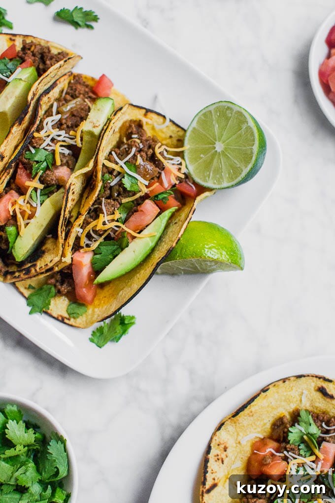 Gluten-Free Beef Tacos: Flavorful Corn Tortilla Recipe 2 Aerial view of a plate of ground beef tacos with limes, a bowl of cilantro, tomatoes, and sliced avocado.