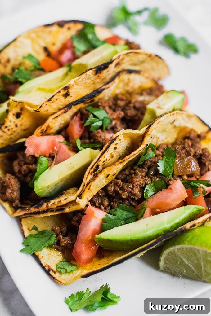 Gluten-Free Beef Tacos: Flavorful Corn Tortilla Recipe 3 Aerial view of ground beef tacos in charred corn tortillas, sliced avocado, diced tomatoes, and chopped cilantro.
