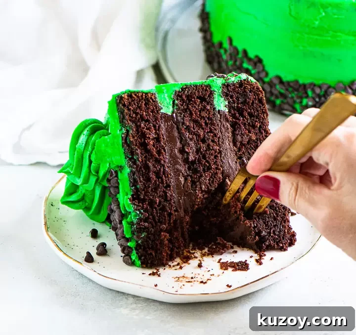 Decadent Chocolate Mint Cake Recipe with Fudgy Frosting 7 slice of chocolate mint cake on a plate with a hand reaching int with a fork to take a bite