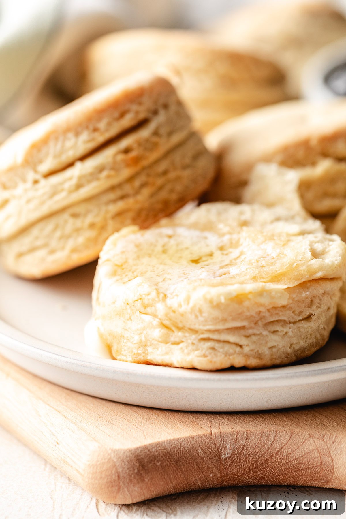 Close up of a tall, flaky homemade biscuit with butter on top, showing distinct layers on the side.