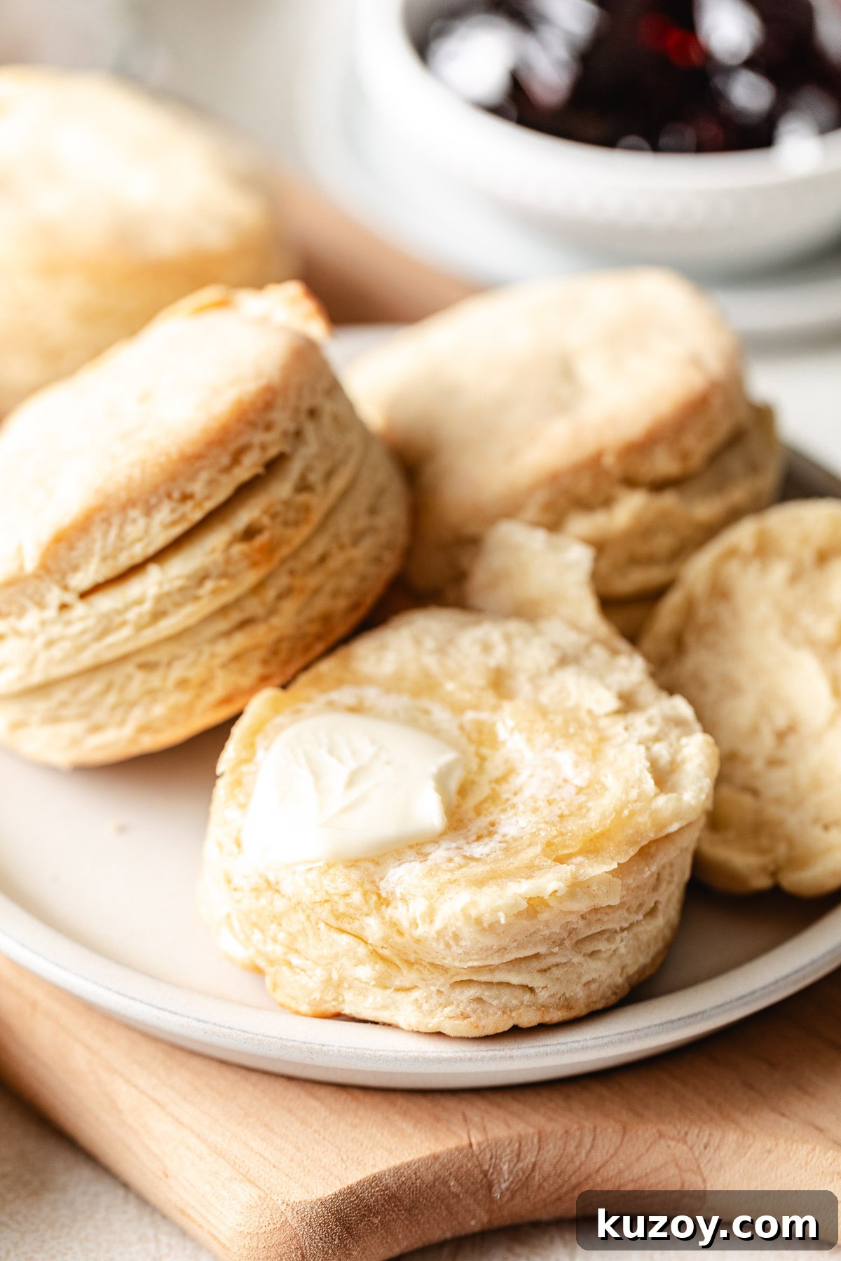Split homemade buttermilk biscuit with a pat of butter melting inside, served on a plate with jam in the background