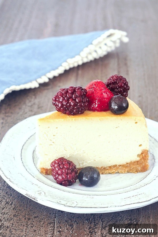 Vegan New York Cheesecake @spabettie #vegan one slice of vegan cheesecake on a rustic white plate with fresh blackberries, blueberries and a strawberry