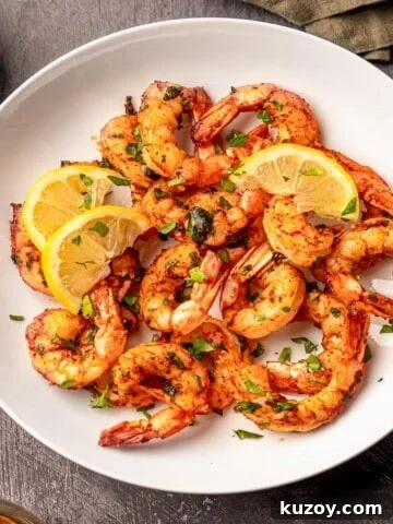 A white bowl filled with shrimp topped with lemon slices next to a green napkin.