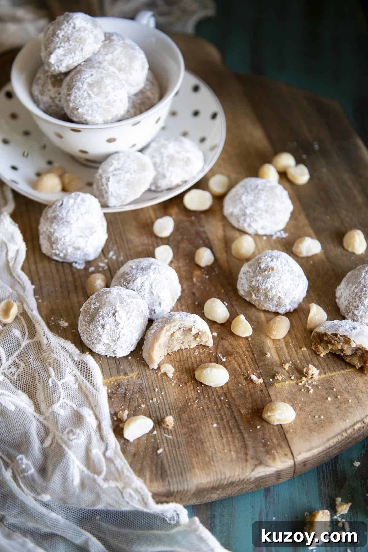 Snowball cookies spread on a wooden board with macadamia nuts.