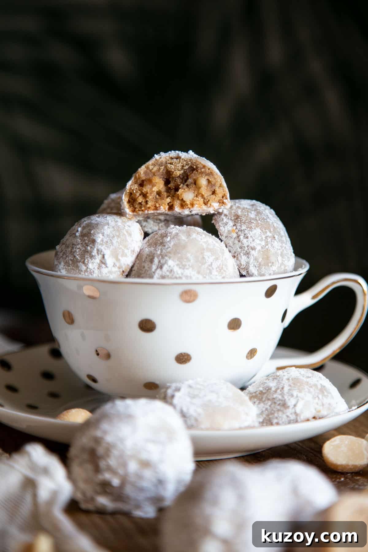 Snowball cookies in a tea cup with one half eaten cookie at top.