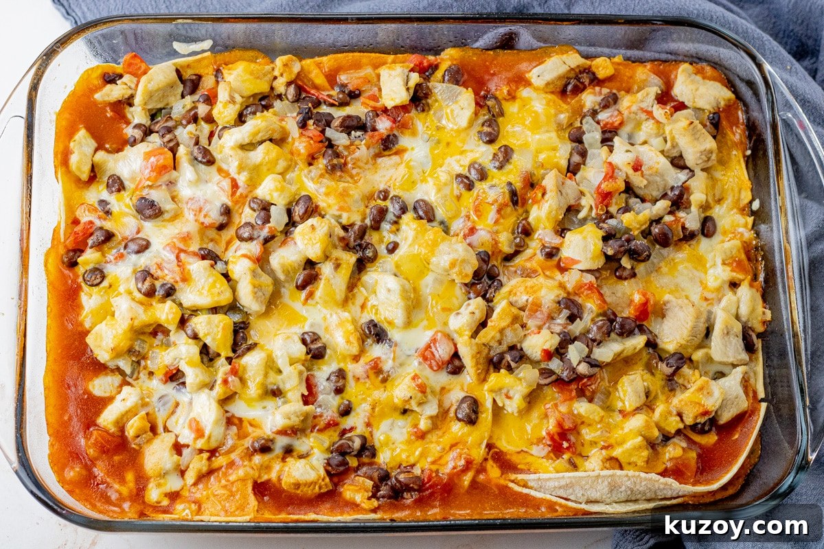 a glass baking dish filled with layers of tortillas, enchilada sauce, chicken, black beans