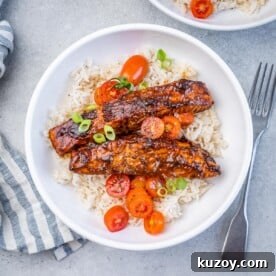 A white bowl with rice topped with 2 salmon fillets and tomato salad garnish.