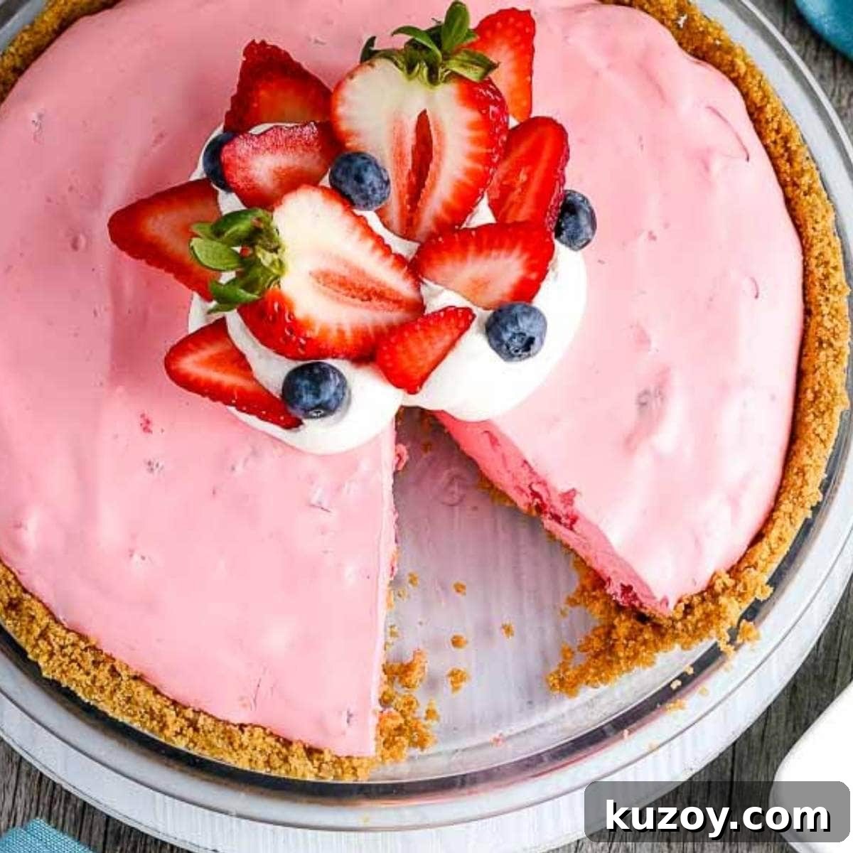 Closeup of a Strawberry Jello Pie garnished with fresh berries and whipped cream with a slice missing.