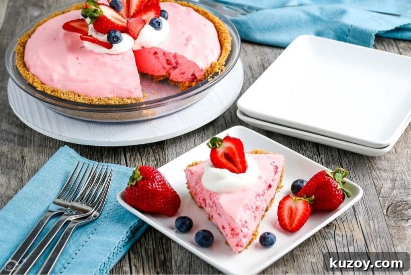 A slice of creamy Cool Whip jello pie garnished with fresh berries and whipped topping on a white plate with full pie, napkin, cutlery & plates in the background.