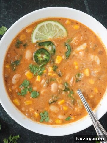 Vegan white bean chili in a bowl with a spoon and garnished with chopped cilantro leaves and a lime wedge.