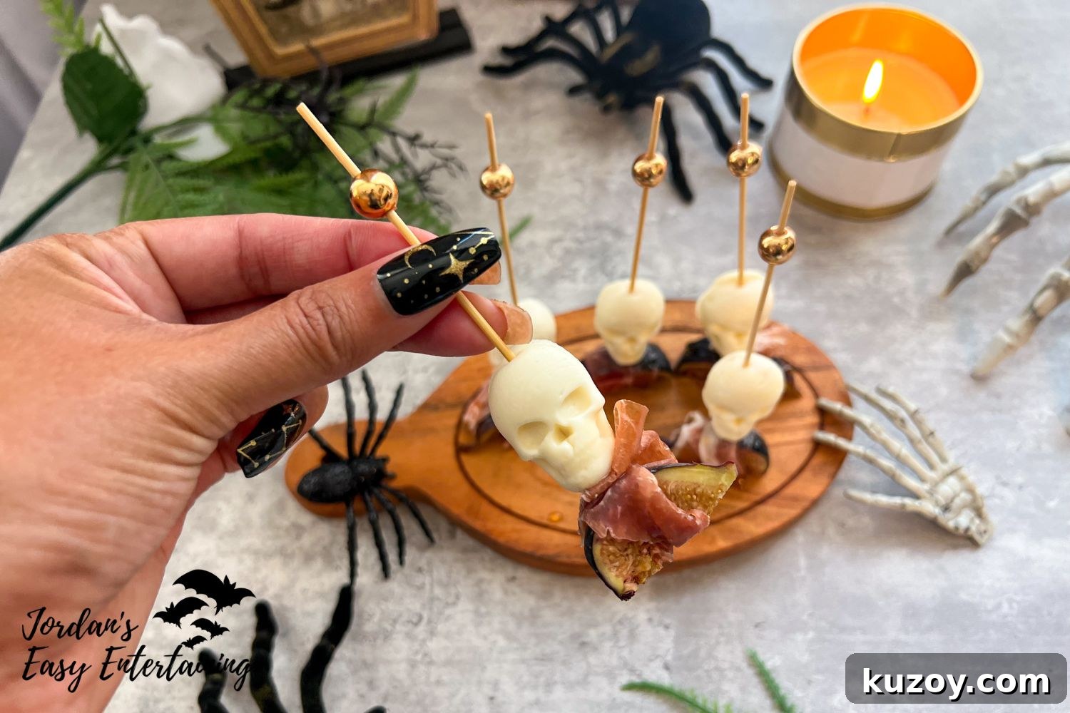 Prosciutto-Wrapped Figs with Honey and Skull Cheese Skewers 3 Close-up of Halloween appetizers featuring mozzarella skull cheese bites skewered with gold cocktail picks, wrapped in prosciutto, and paired with fresh figs on a wooden serving board.