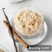 Creamy Dairy-Free Vegan Rice Pudding Recipe 4 A glass bowl of vegan rice pudding with a cinnamon stick and vanilla bean next to it.