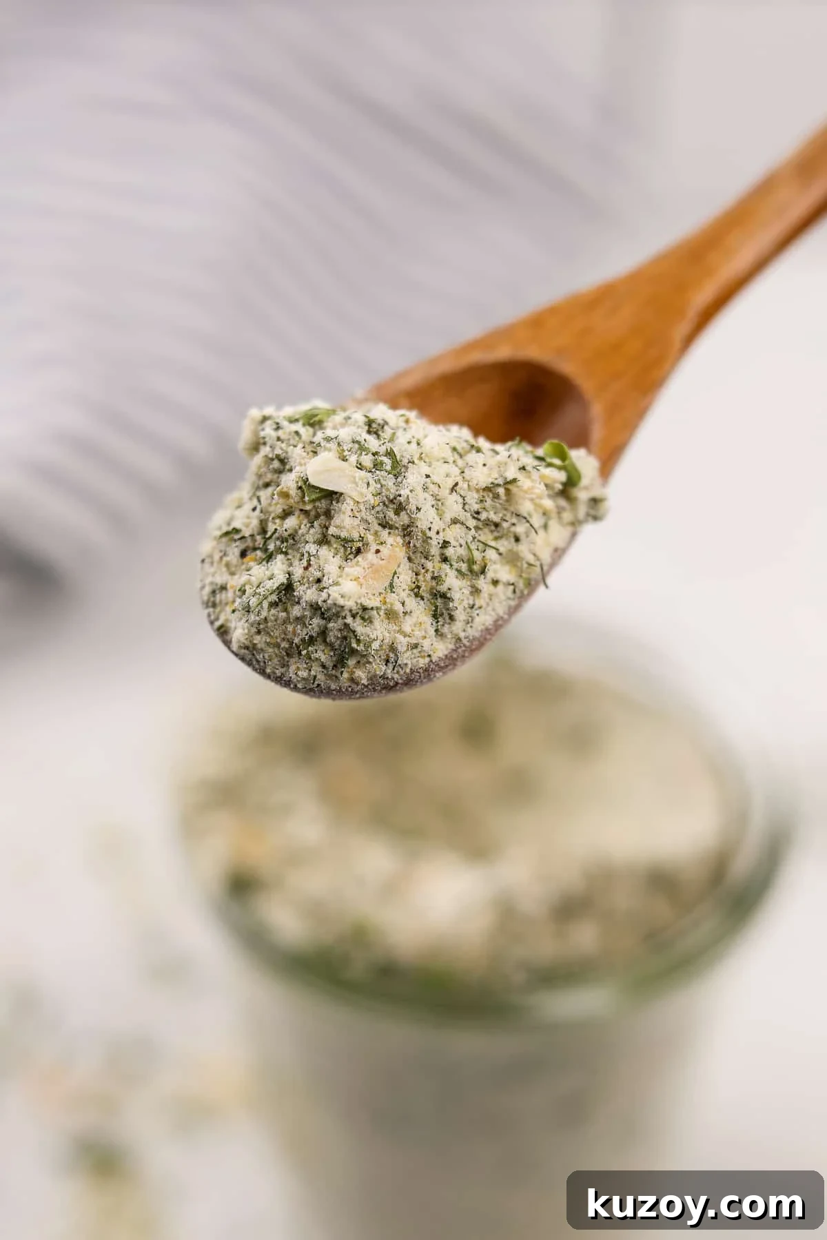 Homemade Ranch Seasoning Mix Recipe for Dips & Dressings 10 A small wooden spoon scooping out ranch seasoning from a jar.