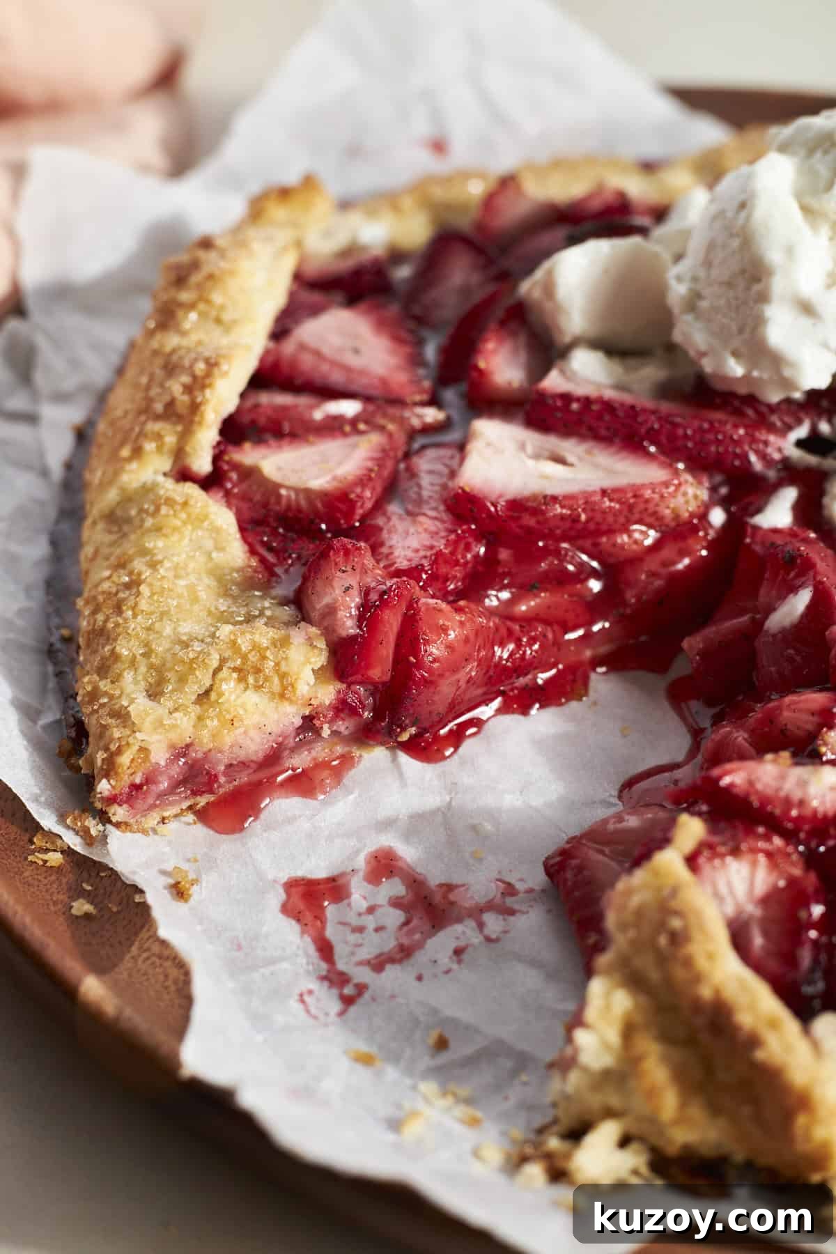 A slice of Sourdough Discard Strawberry Galette on white parchment paper with an ice cream topping. 