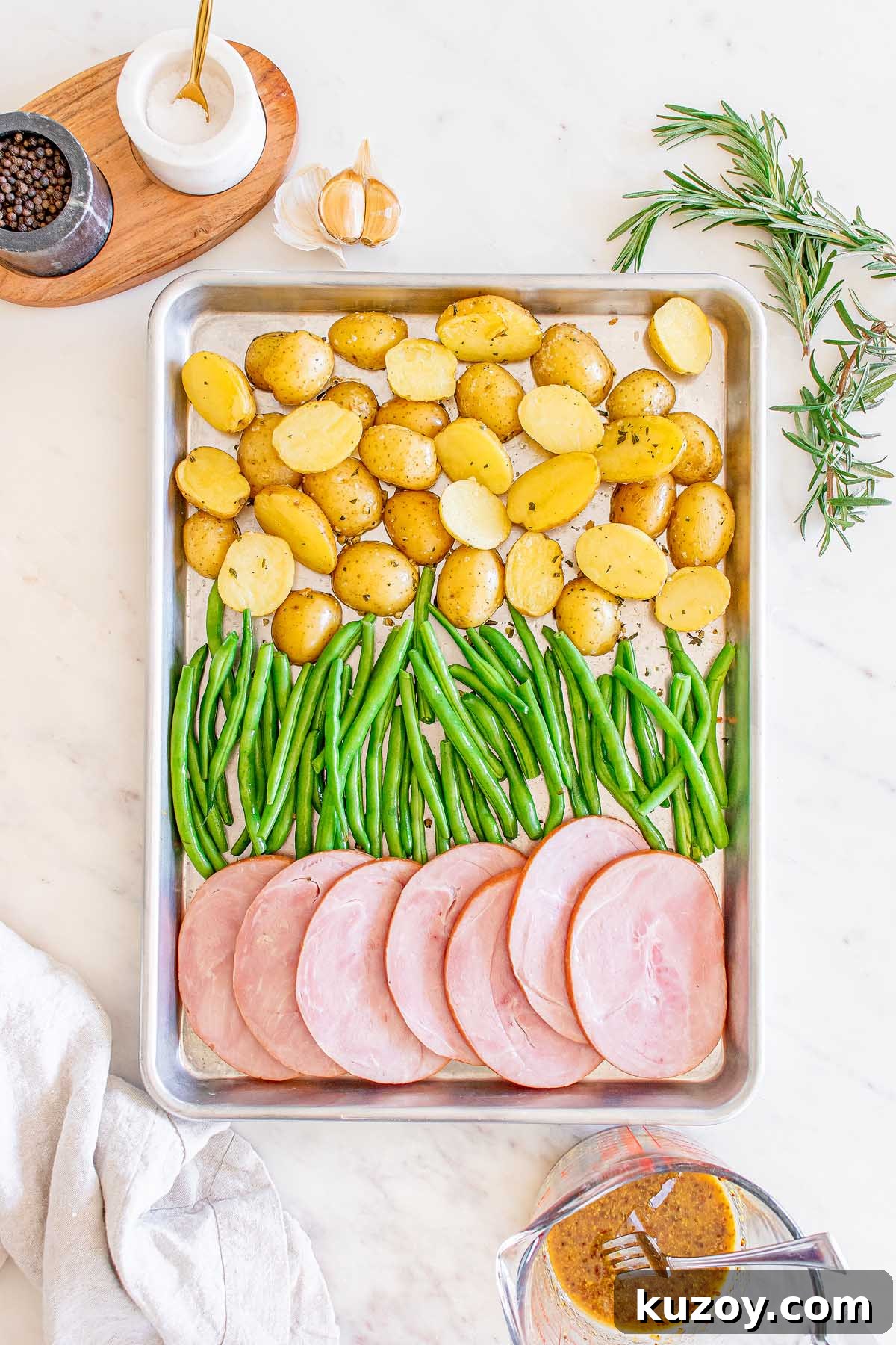 One-Pan Baked Ham Dinner with Roasted Vegetables 14 Ham, green beans and halved potatoes arranged on a baking sheet.