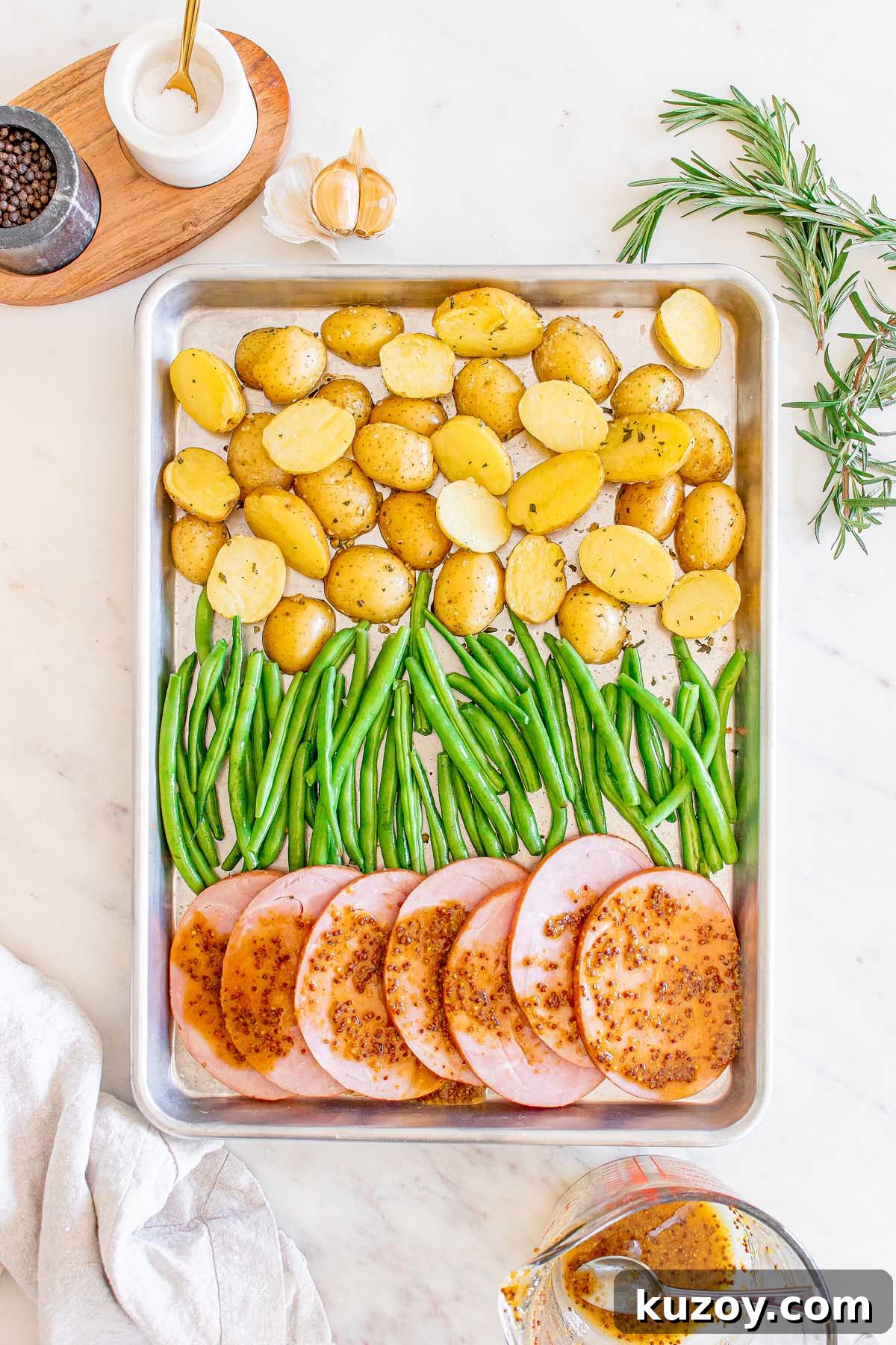 One-Pan Baked Ham Dinner with Roasted Vegetables 15 Baking sheet with ham, green beans and potatoes, with seasonings nearby.