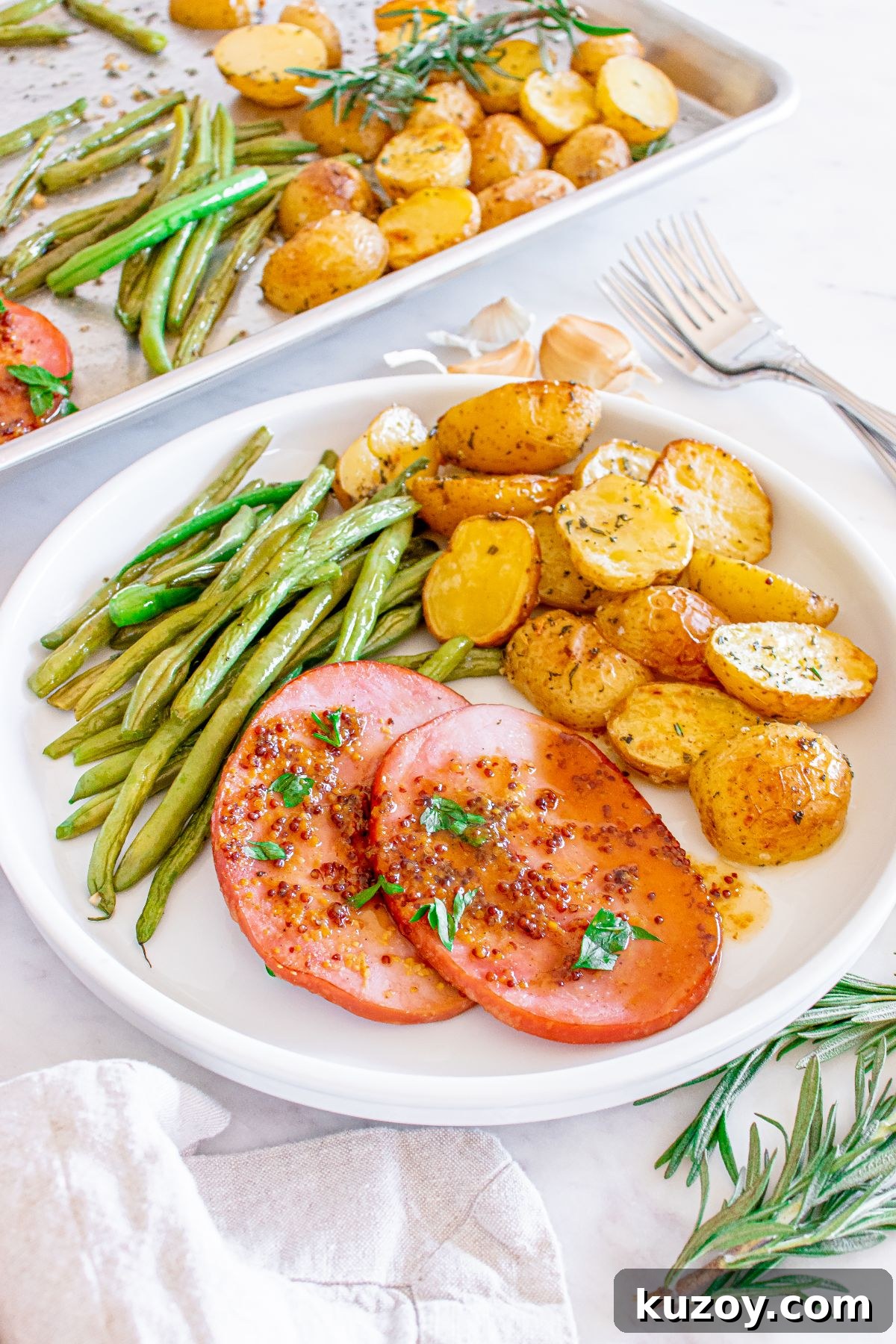 One-Pan Baked Ham Dinner with Roasted Vegetables 17 A plate with green beans, roasted potatoes and two slices of ham garnished with herbs.