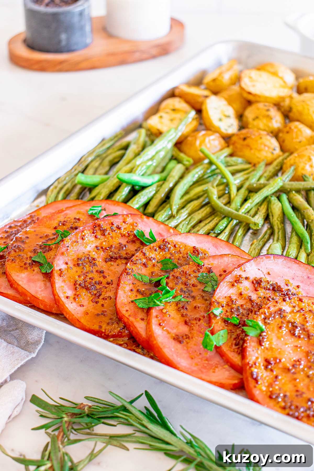 One-Pan Baked Ham Dinner with Roasted Vegetables 3 Sliced ham with herbs, green beans and roasted potatoes on a tray.