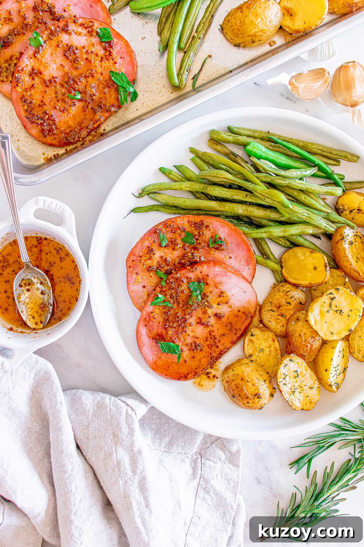 One-Pan Baked Ham Dinner with Roasted Vegetables 6 Plate with sliced ham, roasted potatoes and green beans with a bowl of sauce nearby.
