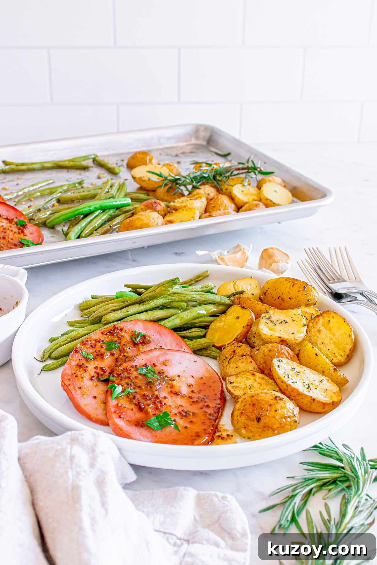One-Pan Baked Ham Dinner with Roasted Vegetables 7 Slices of ham with roasted potatoes and green beans on a plate.