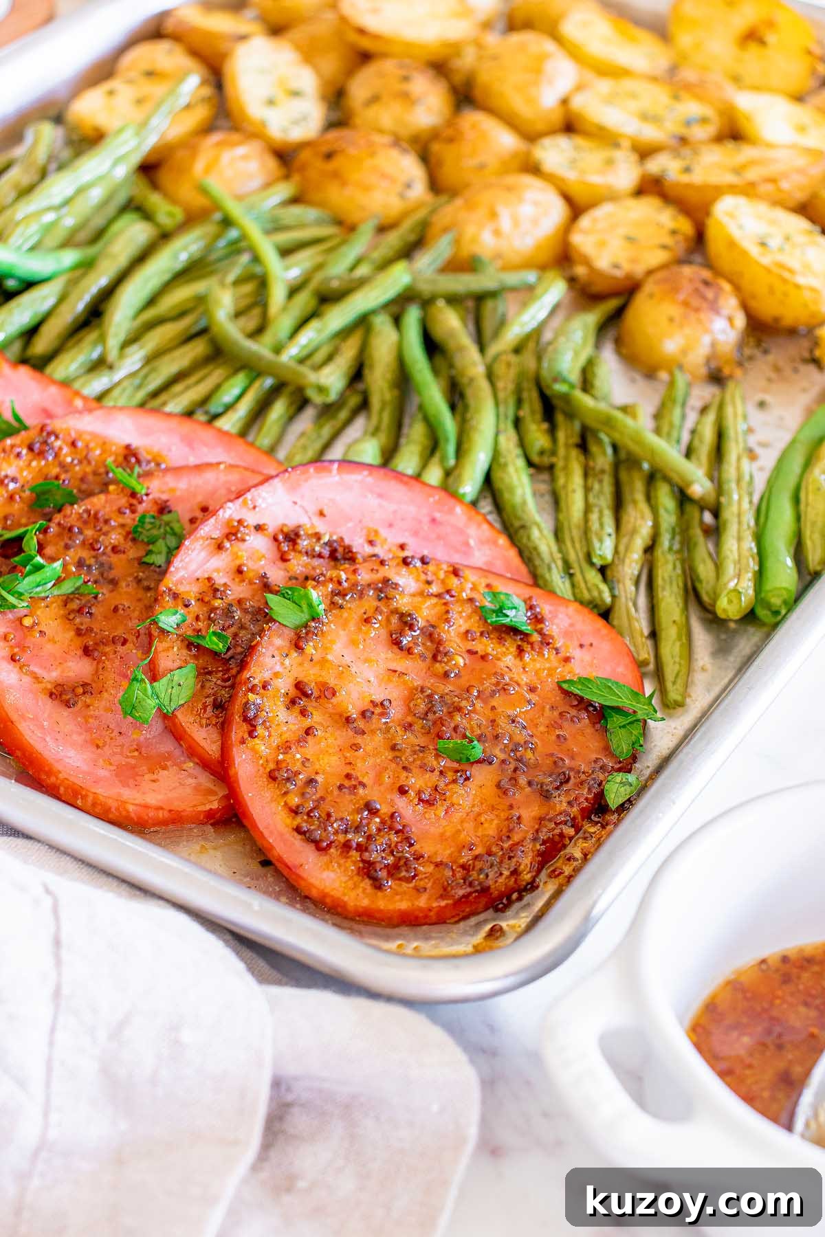 One-Pan Baked Ham Dinner with Roasted Vegetables 10 Baked ham slices with mustard glaze, roasted green beans and potatoes on a sheet pan.