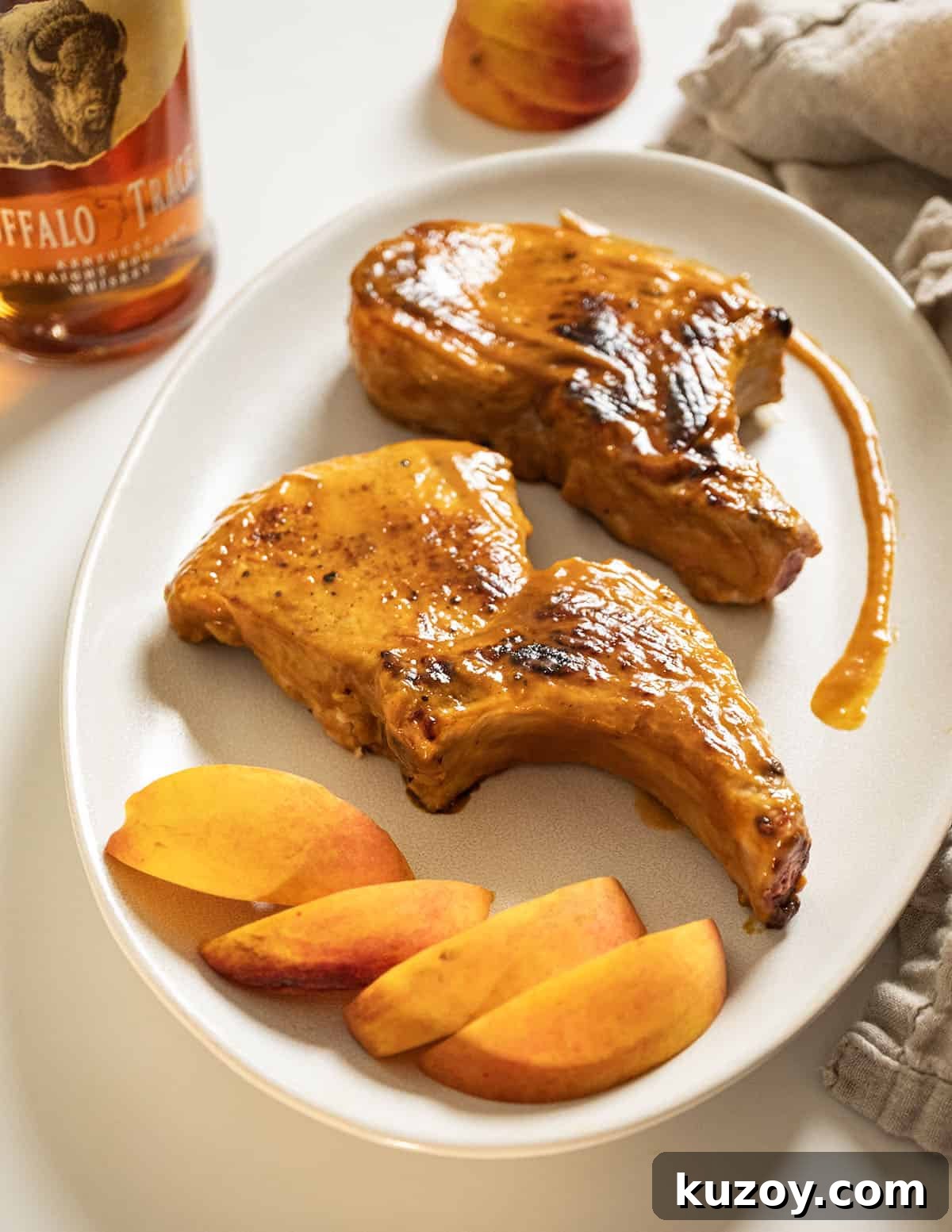 Peach Bourbon Glazed Pork Chops with Pan Sauce 2 Bourbon peach glazed pork chops on a plate garnished with peaches and extra sauce.