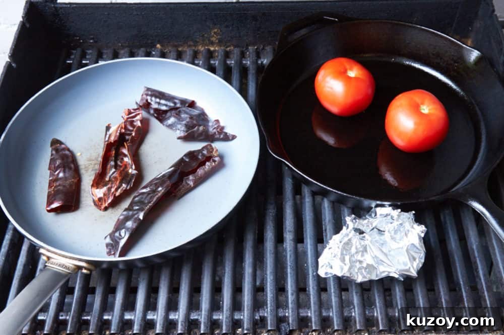 Orange-Almond Mole Sauce: Quick Recipe for Rich, Zesty Flavor 5 A grill with two skillets, one containing dried chiles, the other containing tomatoes. A foil pouch with roasting garlic sits beside them.