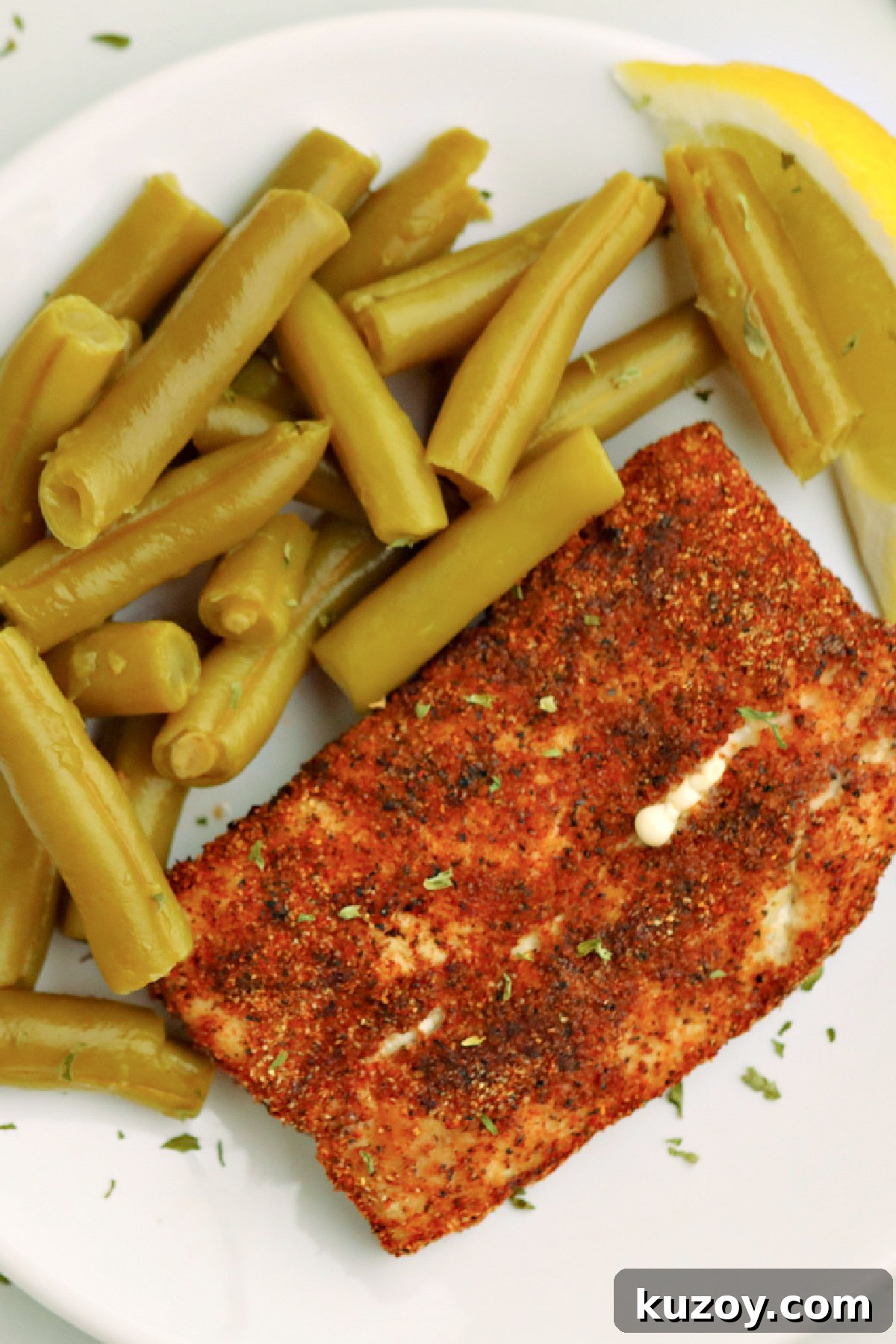 Overhead shot of mahi mahi on a plate with green beans and a lemon slice. 