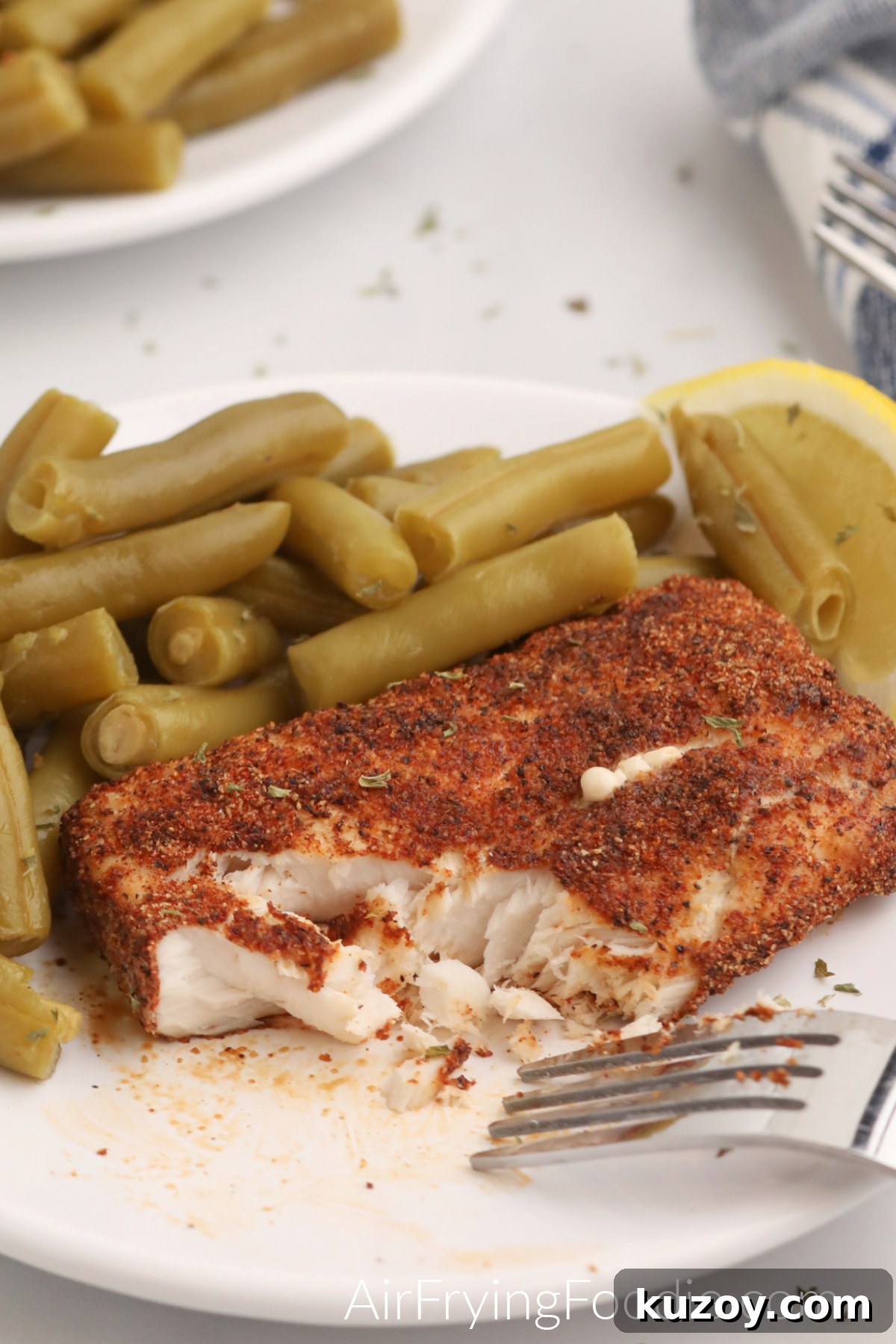 Close up of Mahi Mahi on a white plate with green beans and a lemon slice. 