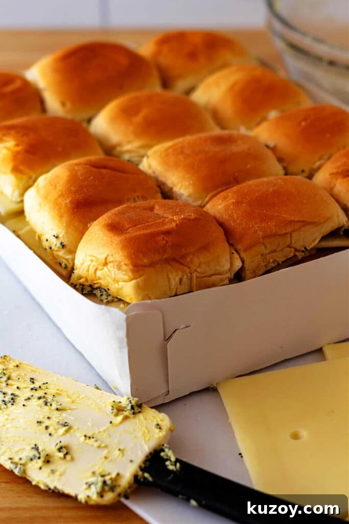 A white paper tray of 12 slider buns filled with poppy seed and butter filling, ham, and cheese.