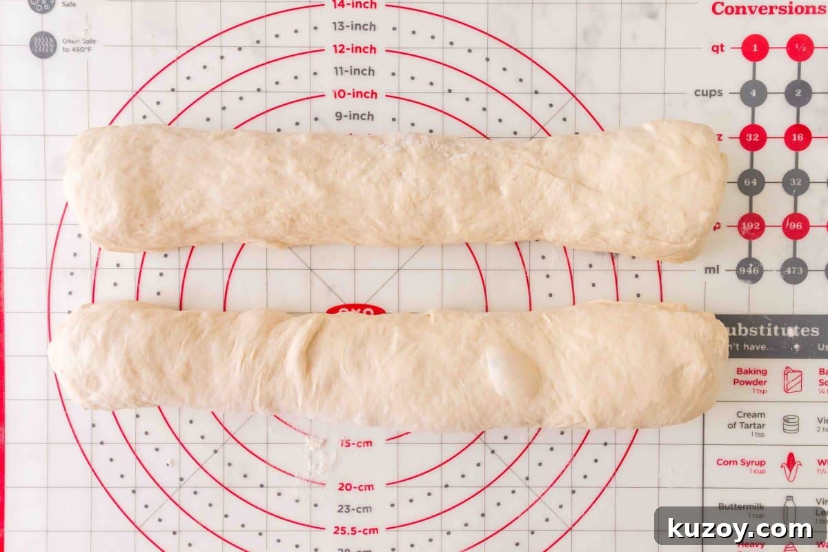 Two baguettes of French bread dough rolled into baguette log shapes on a pastry mat. Hostess At Heart