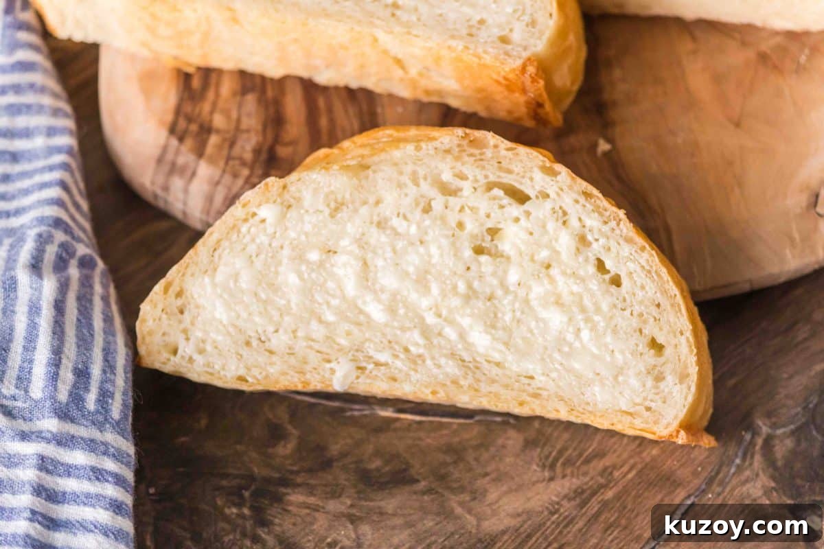 A slice of French Bread from a baguette baked on a baking sheet showing a slightly flatter bottom. Hostess At Heart